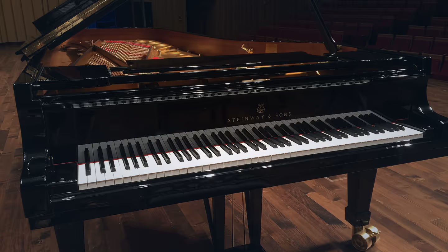 Black Steinway & Sons grand piano with open lid on wooden floor in a concert hall.